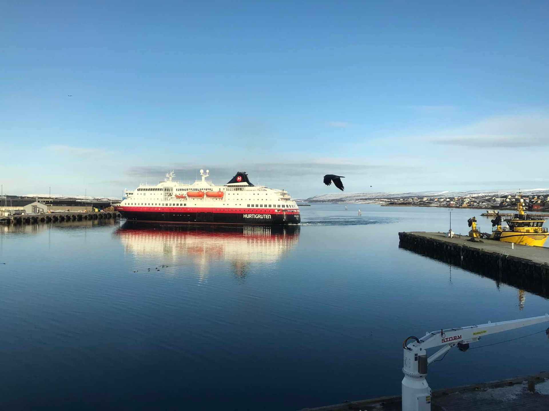 Hurtigrutenskip i rolig havn med speiling i sjøen, snødde bakker i bakgrunnen
